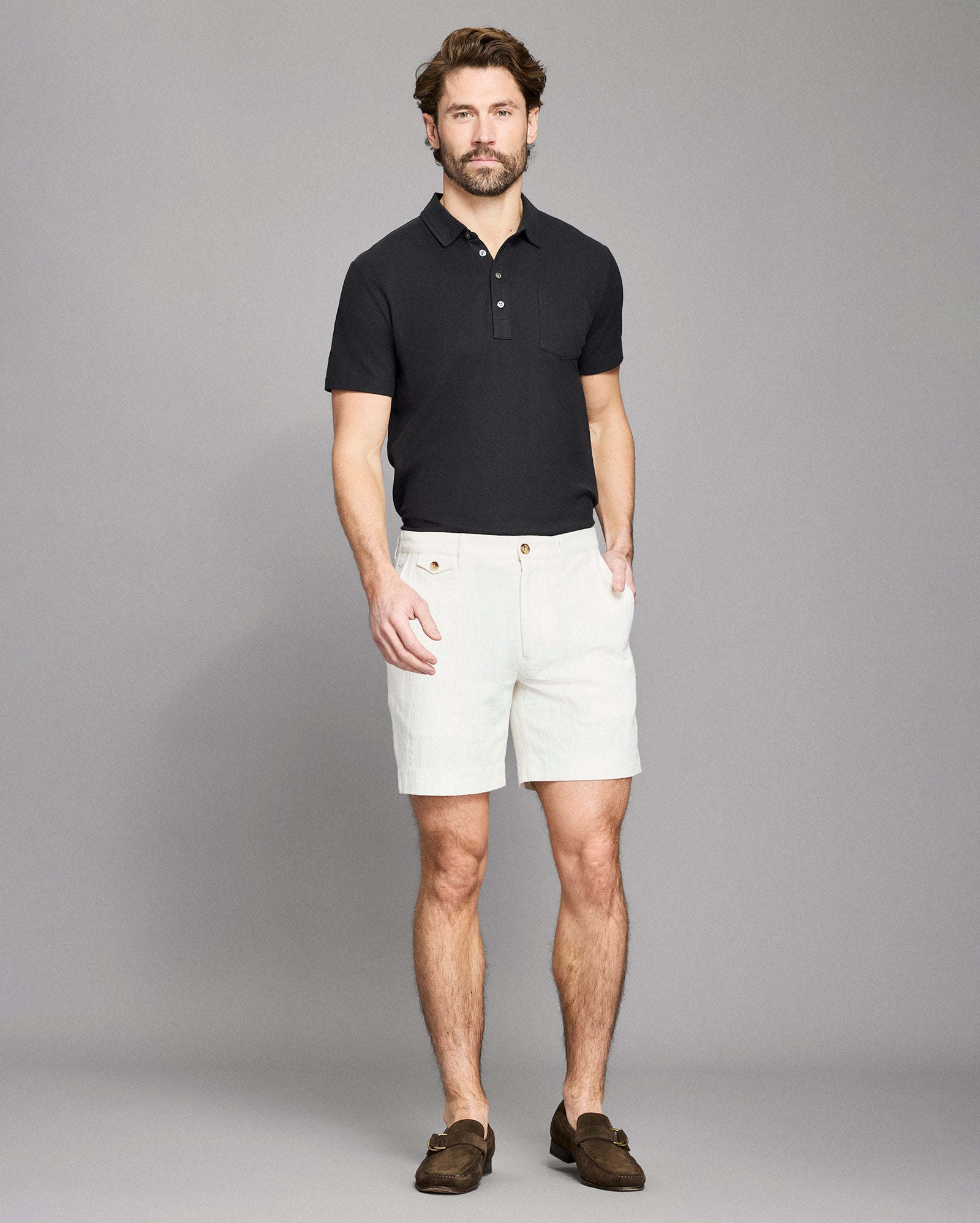 Man wearing a black polo shirt and white shorts against a gray background