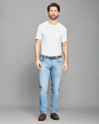 Man wearing a white t-shirt and light blue jeans on a gray background