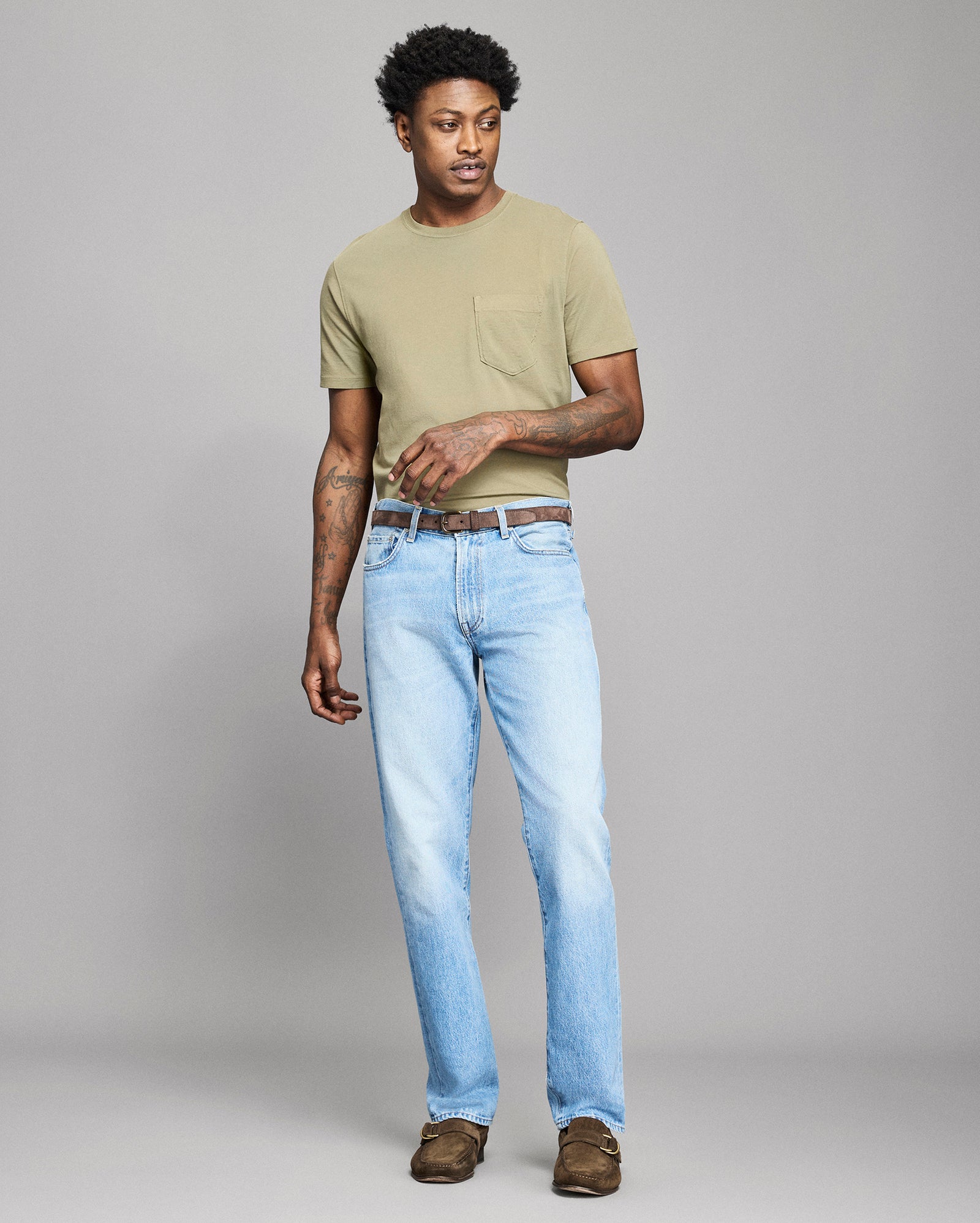 Man wearing a beige t-shirt and light blue jeans on a gray background