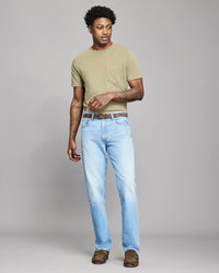 Man wearing a beige t-shirt and light blue jeans on a gray background