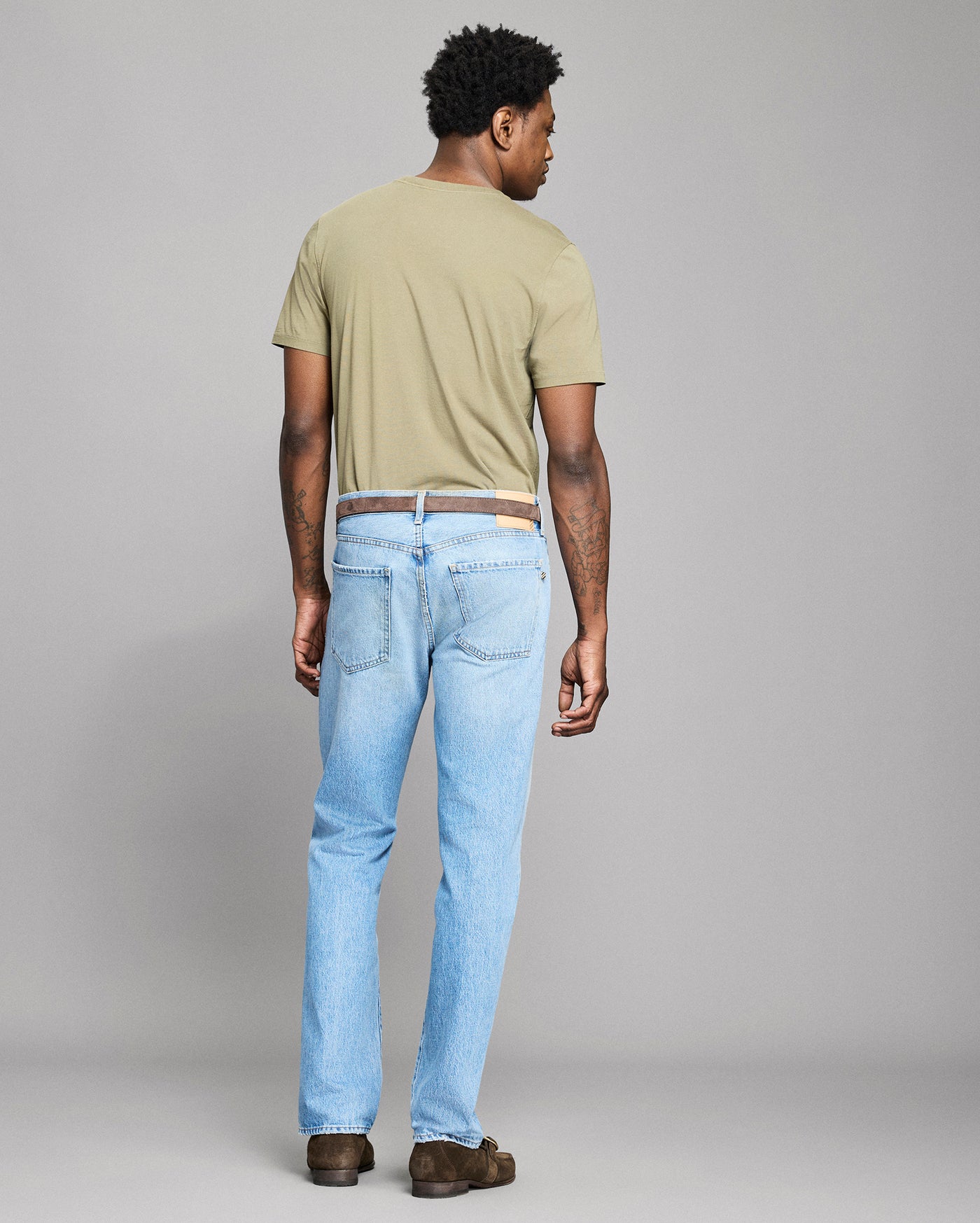 Man wearing a light green t-shirt and light blue jeans against a gray background