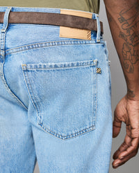 Light blue jeans with a brown belt and visible brand label, on a neutral background.