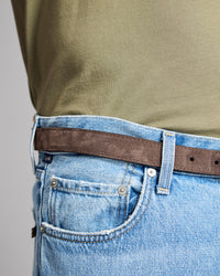 Close-up of blue jeans with a brown belt and green shirt on a gray background