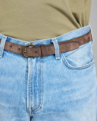 Close-up of blue jeans with a brown belt and green shirt.