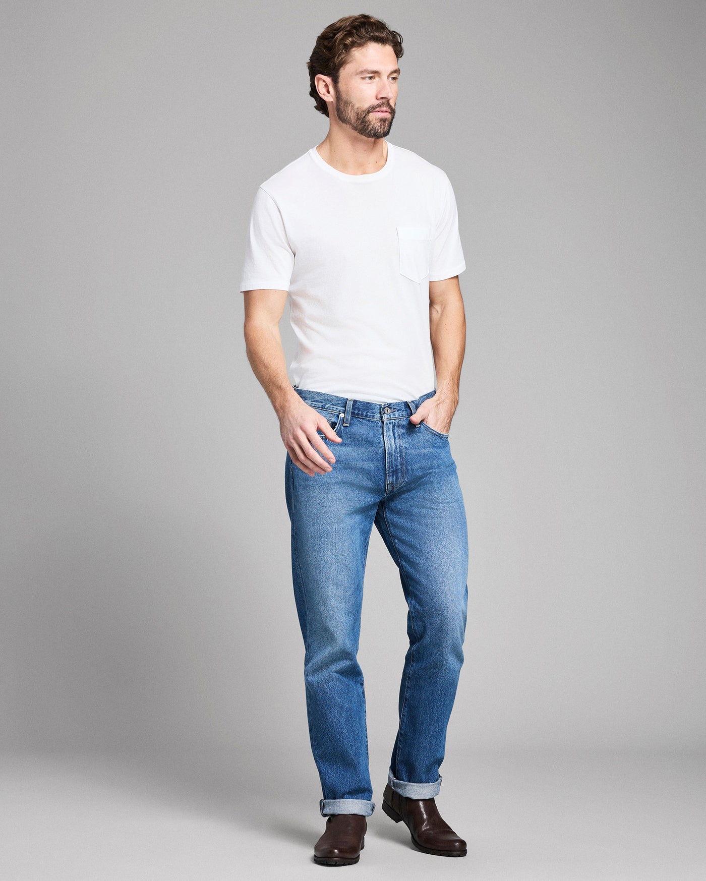 Man wearing a white t-shirt and blue jeans on a gray background