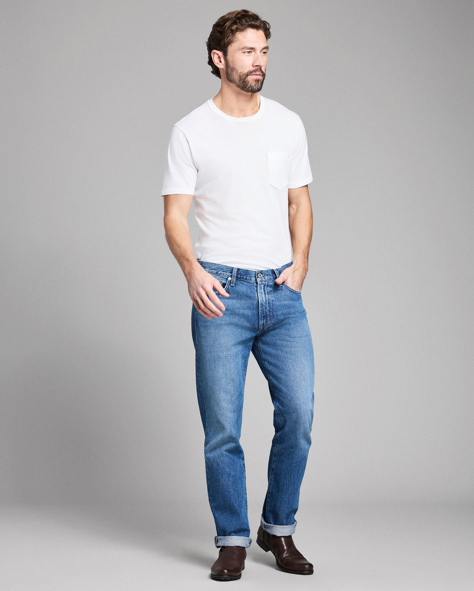 Man wearing a white t-shirt and blue jeans on a gray background