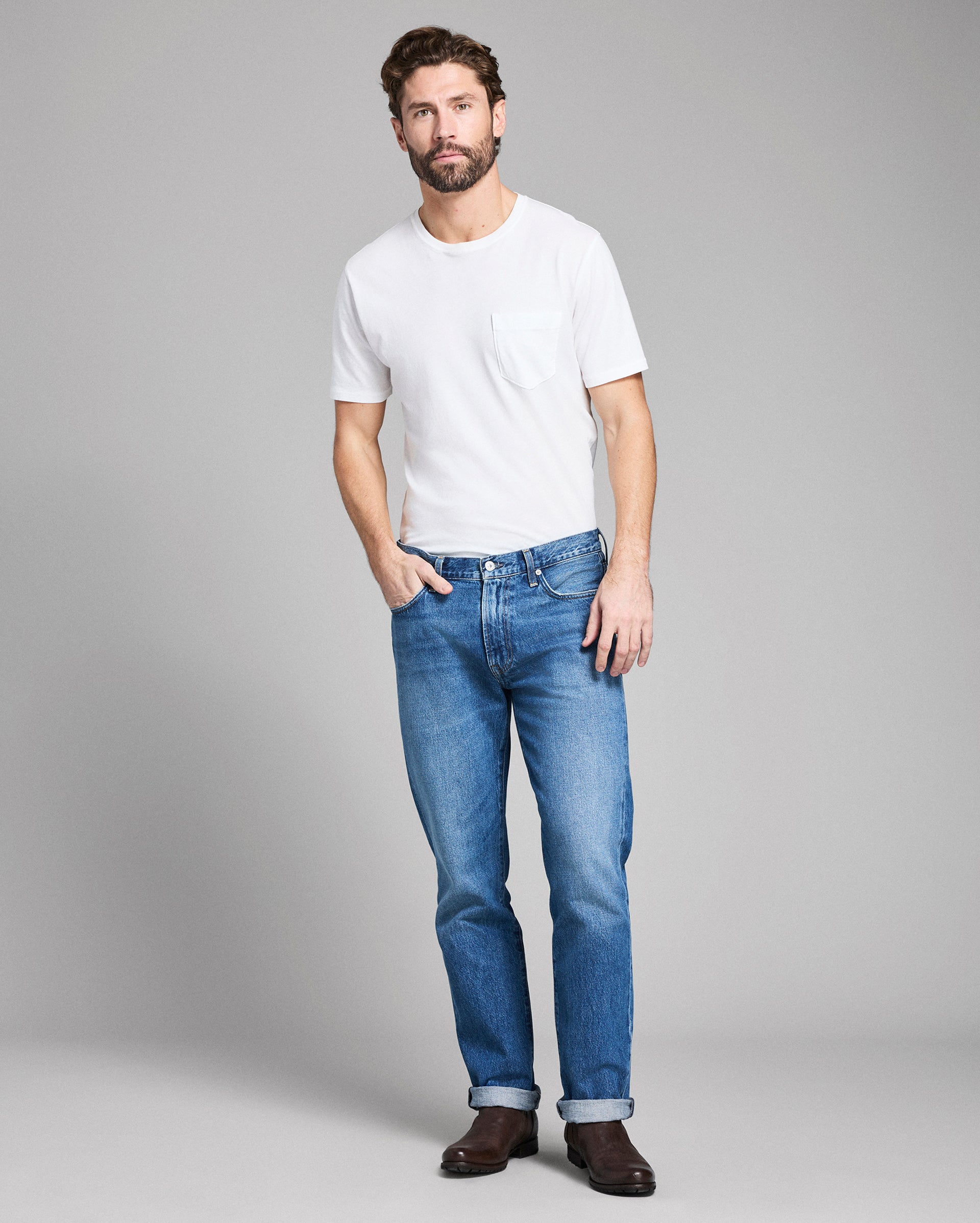 Man wearing a white t-shirt and blue jeans against a gray background