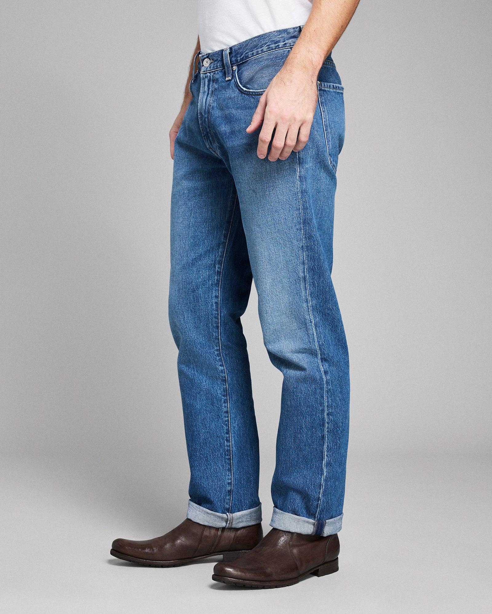 Person wearing blue jeans and brown shoes on a gray background