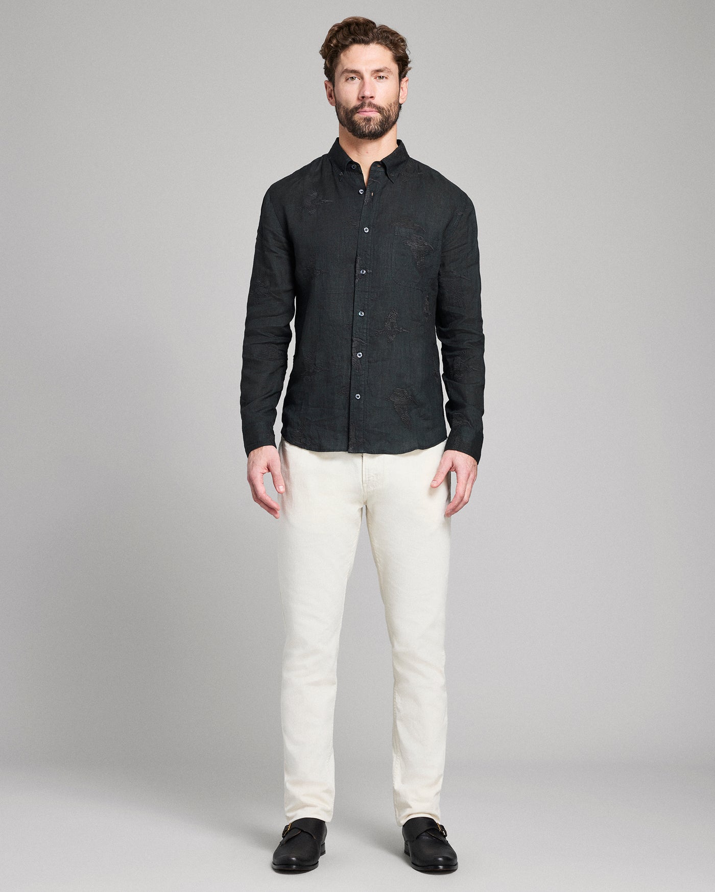 Man wearing a black textured shirt and white pants on a gray background