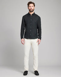 Man wearing a black textured shirt and white pants on a gray background