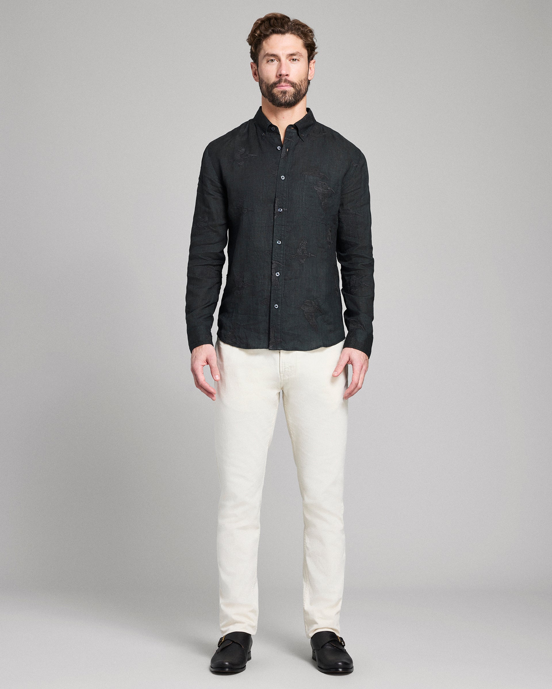 Man wearing a black textured shirt and white pants on a gray background
