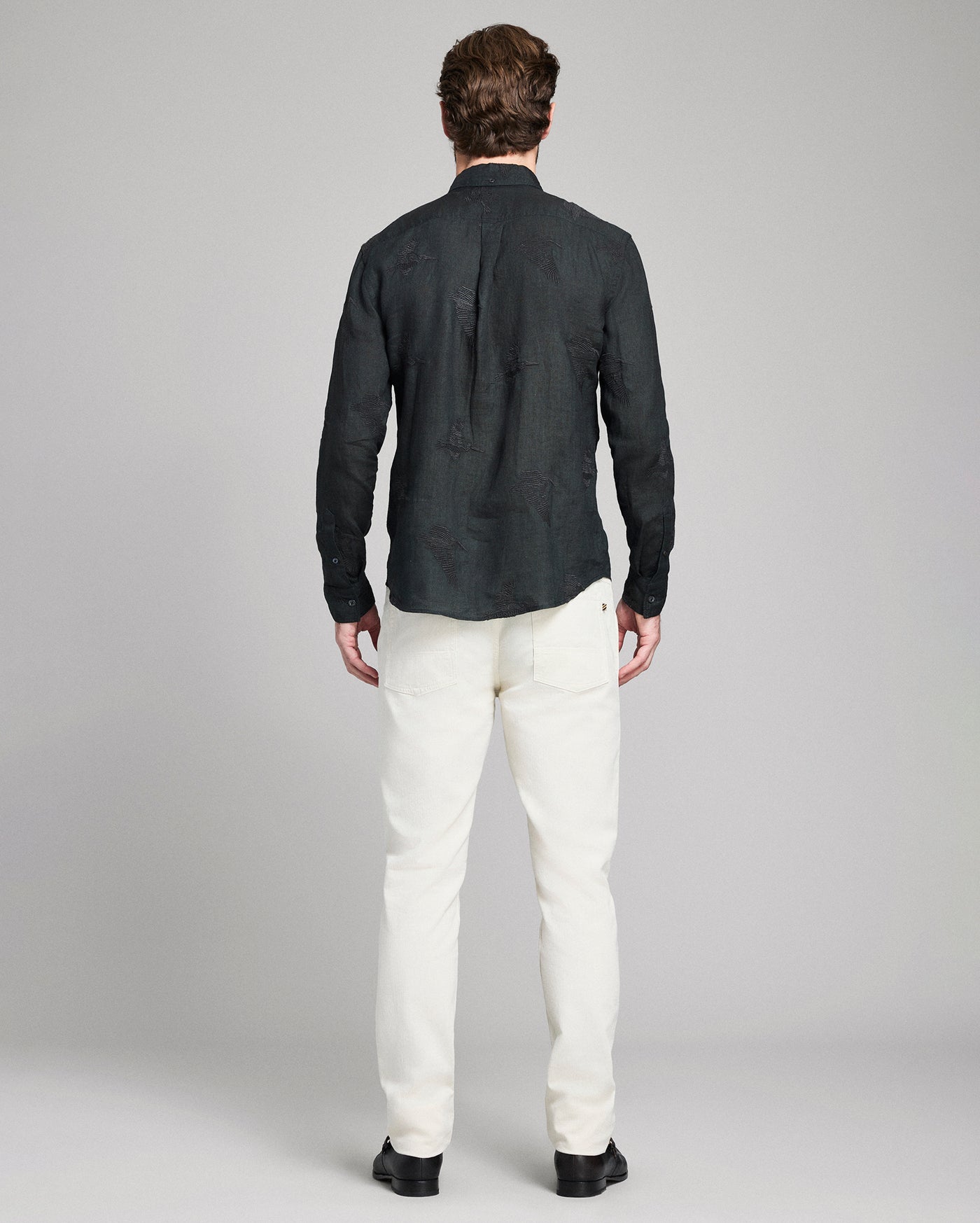 Man wearing a black shirt and white pants on a gray background