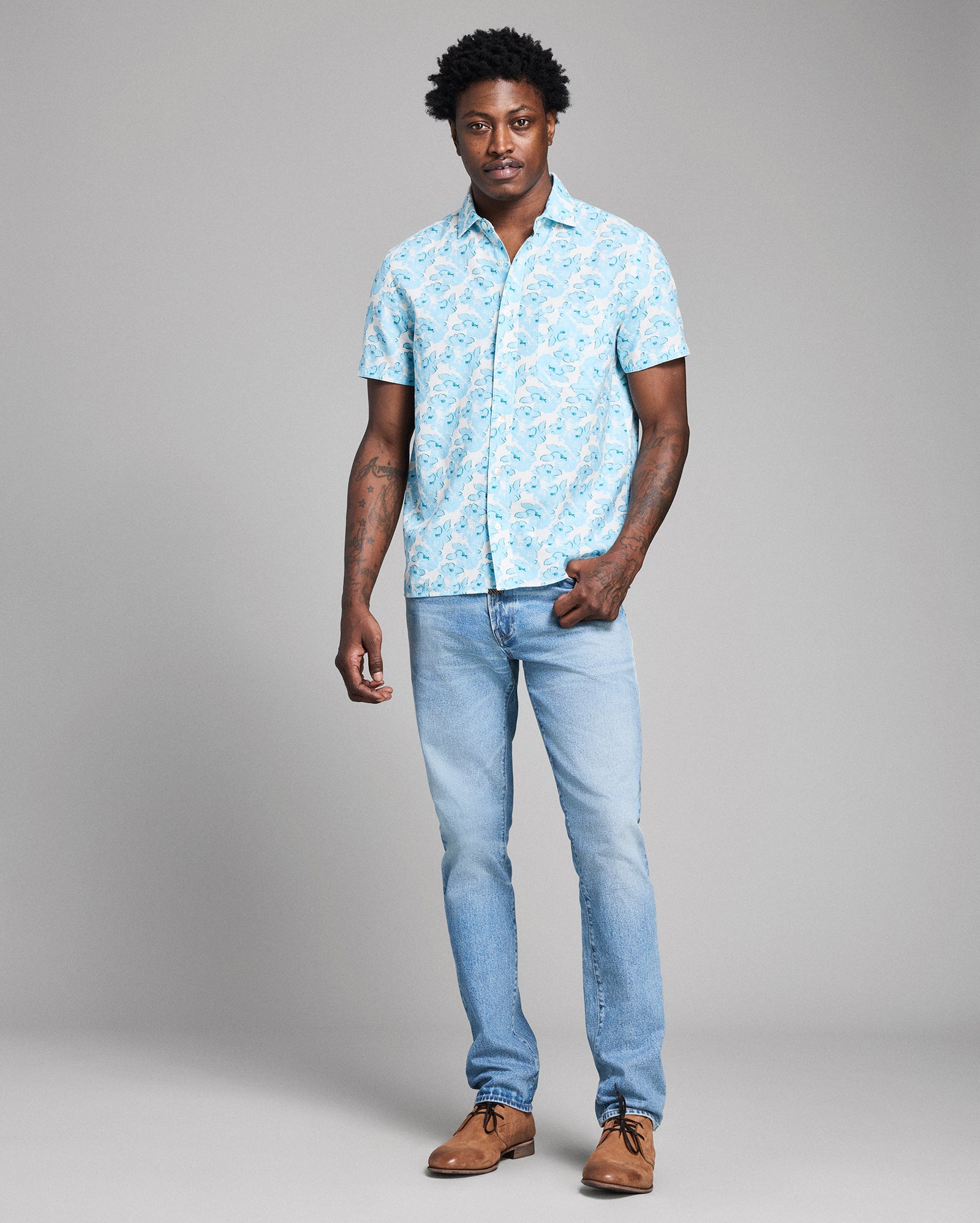 Man wearing a light blue patterned shirt and jeans on a gray background