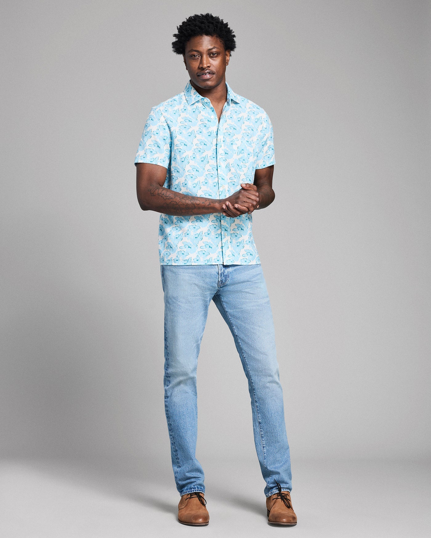 Man wearing a light blue floral shirt and jeans on a gray background