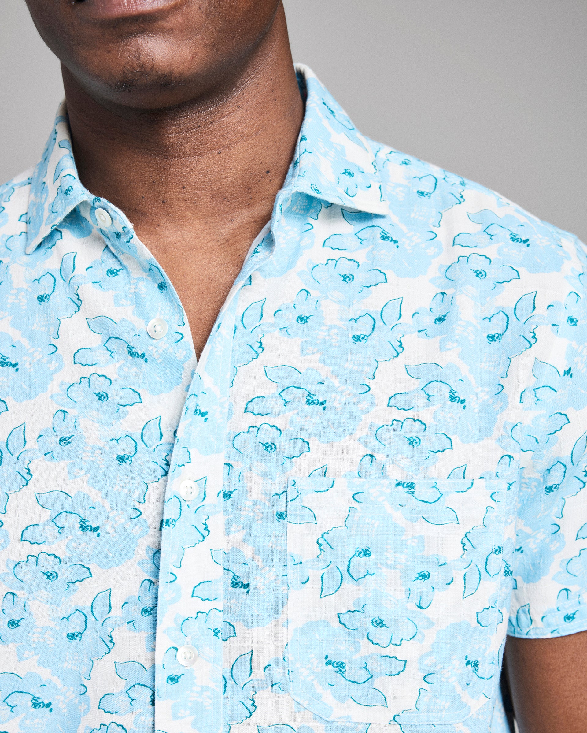 Close-up of a person wearing a light blue floral patterned shirt against a neutral background