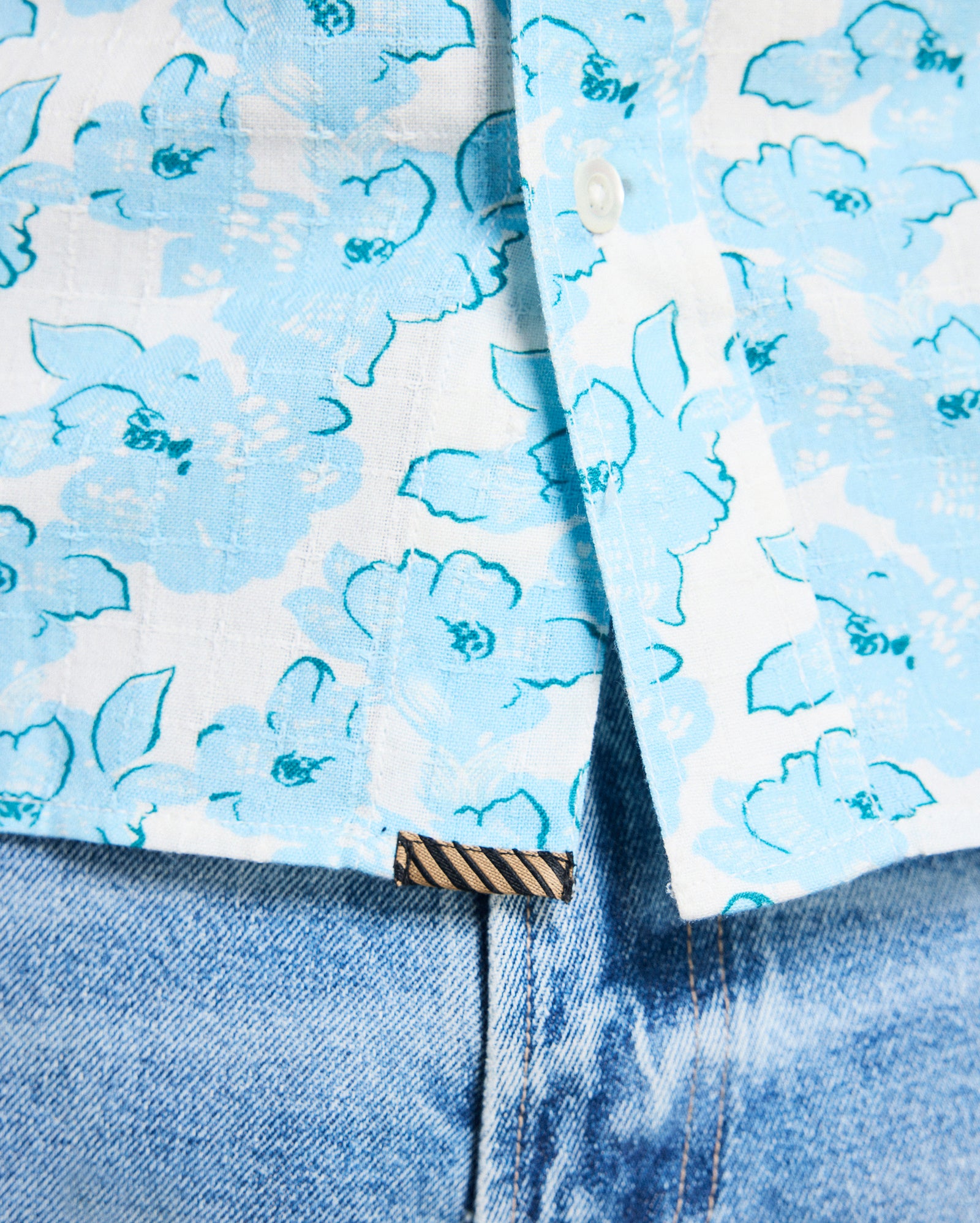 Close-up of a blue floral shirt with a patterned tie and jeans.