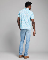 Man wearing a light blue patterned shirt and jeans on a gray background