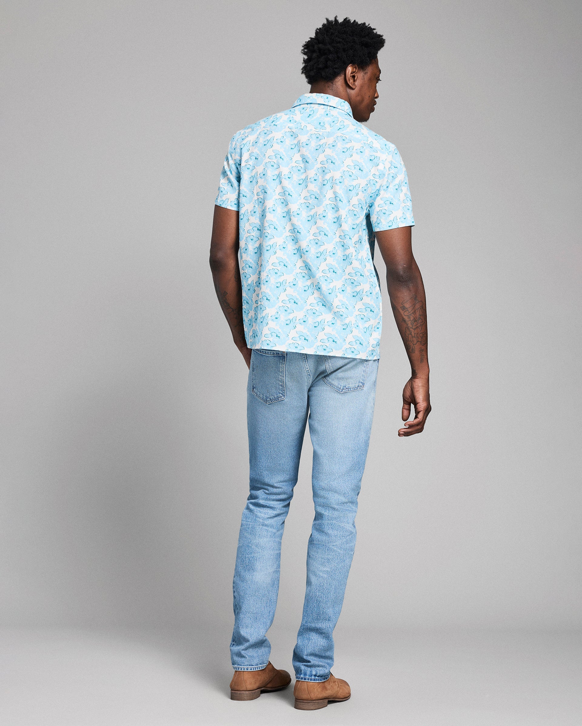 Man wearing a light blue patterned shirt and jeans on a gray background