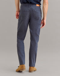 A person wearing dark blue pants, brown shoes, and a navy shirt is shown from the back, standing on a light gray background.