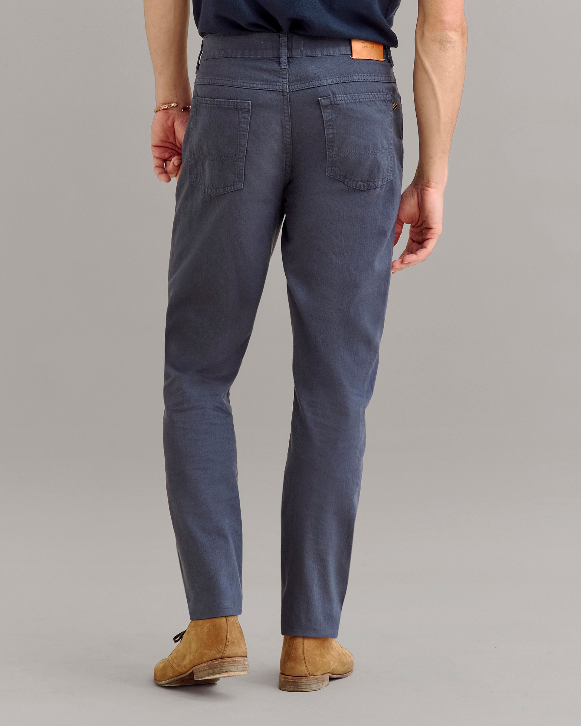 A person wearing dark blue pants, brown shoes, and a navy shirt is shown from the back, standing on a light gray background.