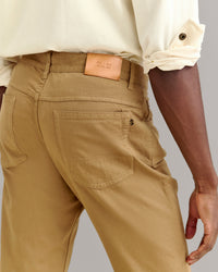 A person wearing tan pants and a light cream shirt with rolled-up sleeves is shown from the back, focusing on the pants pockets and a tan leather patch on the waistband.