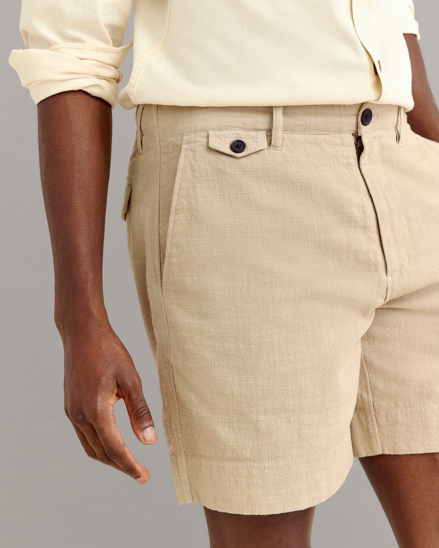 A person wearing a cream-colored long-sleeve shirt and beige textured shorts with side pockets, seen from the waist to mid-thigh against a plain background.