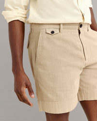 A person wearing a cream-colored long-sleeve shirt and beige textured shorts with side pockets, seen from the waist to mid-thigh against a plain background.