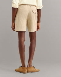 A person wearing beige shorts, a light yellow rolled-up long sleeve shirt, and tan shoes stands facing away, showing the back of the outfit against a plain gray background.