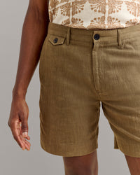 A person wearing textured olive-green shorts with a buttoned waistband and a beige shirt with a brown floral pattern, standing with their left hand relaxed by their side.
