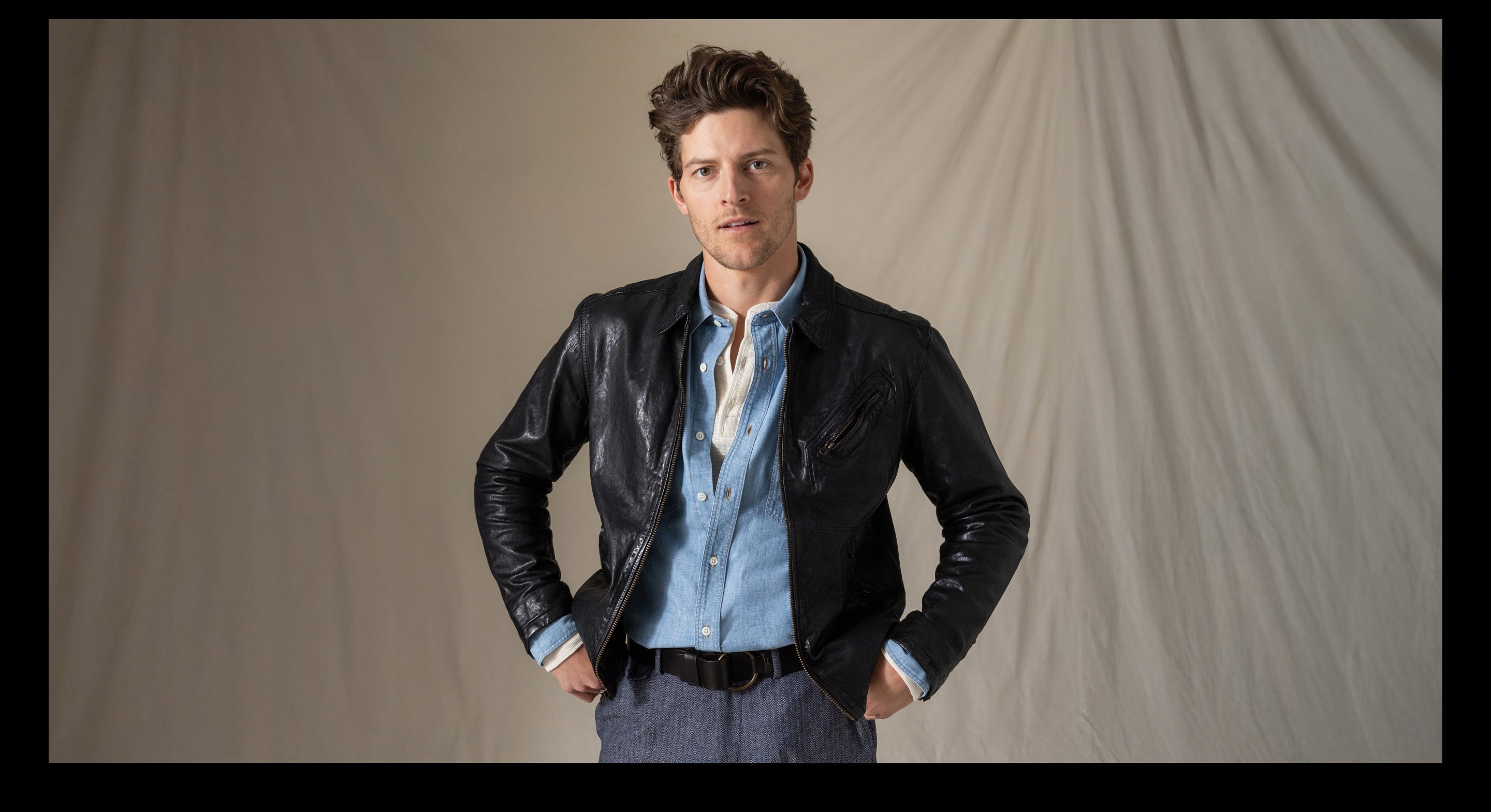 Man wearing a black leather jacket over a blue shirt with a neutral background
