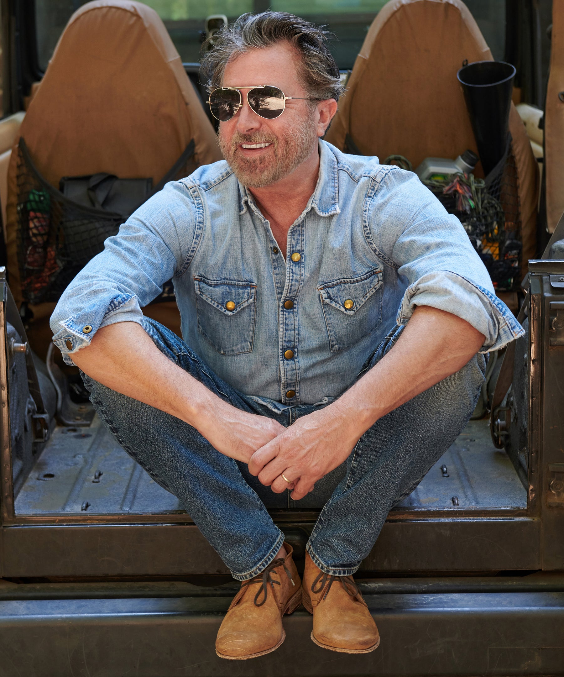 Billy Reid, wearing the Shoals Denim Shirt and Light Indigo Adler Jean, smiles while sitting.