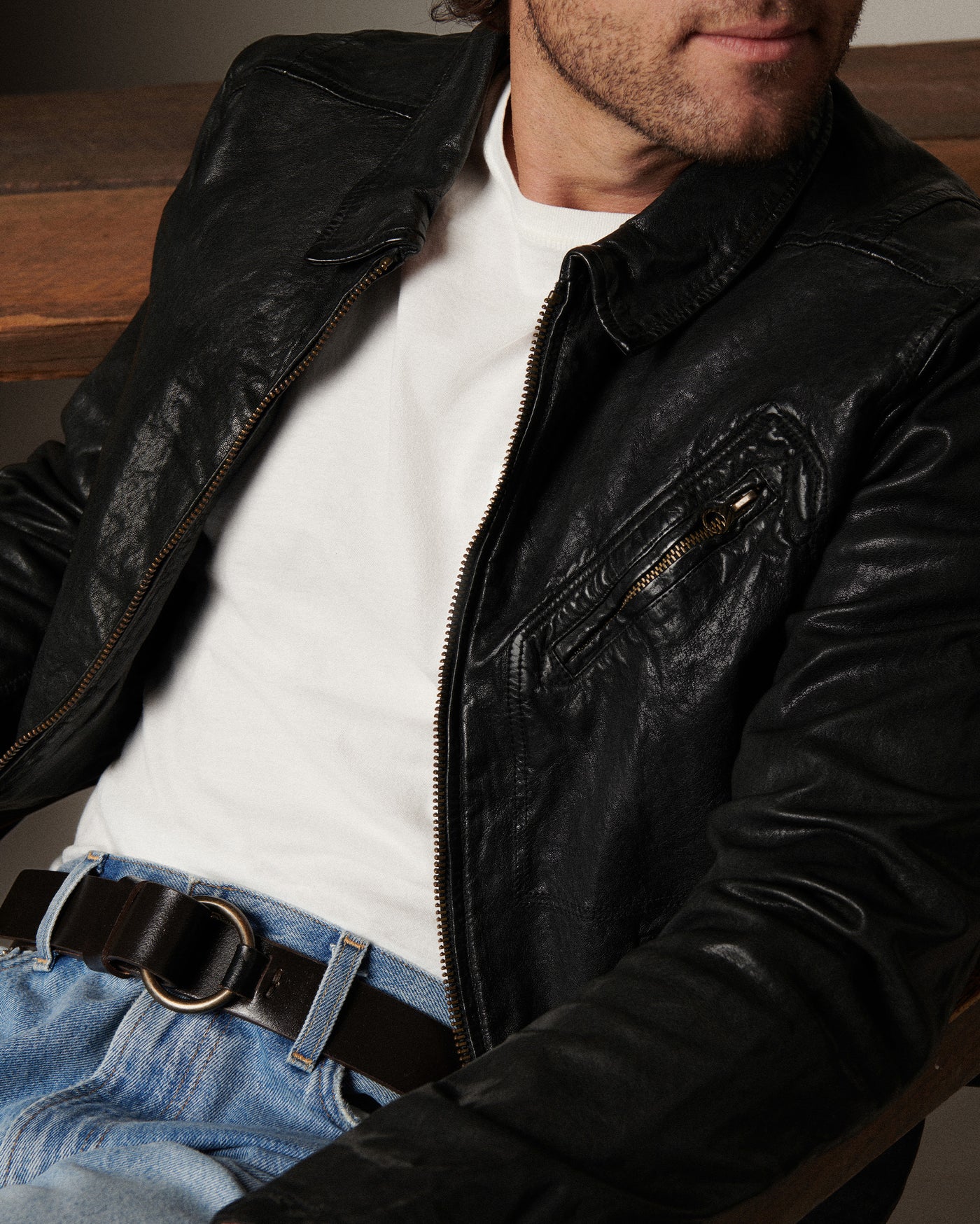 Man wearing a black leather jacket over a white shirt with a wooden background