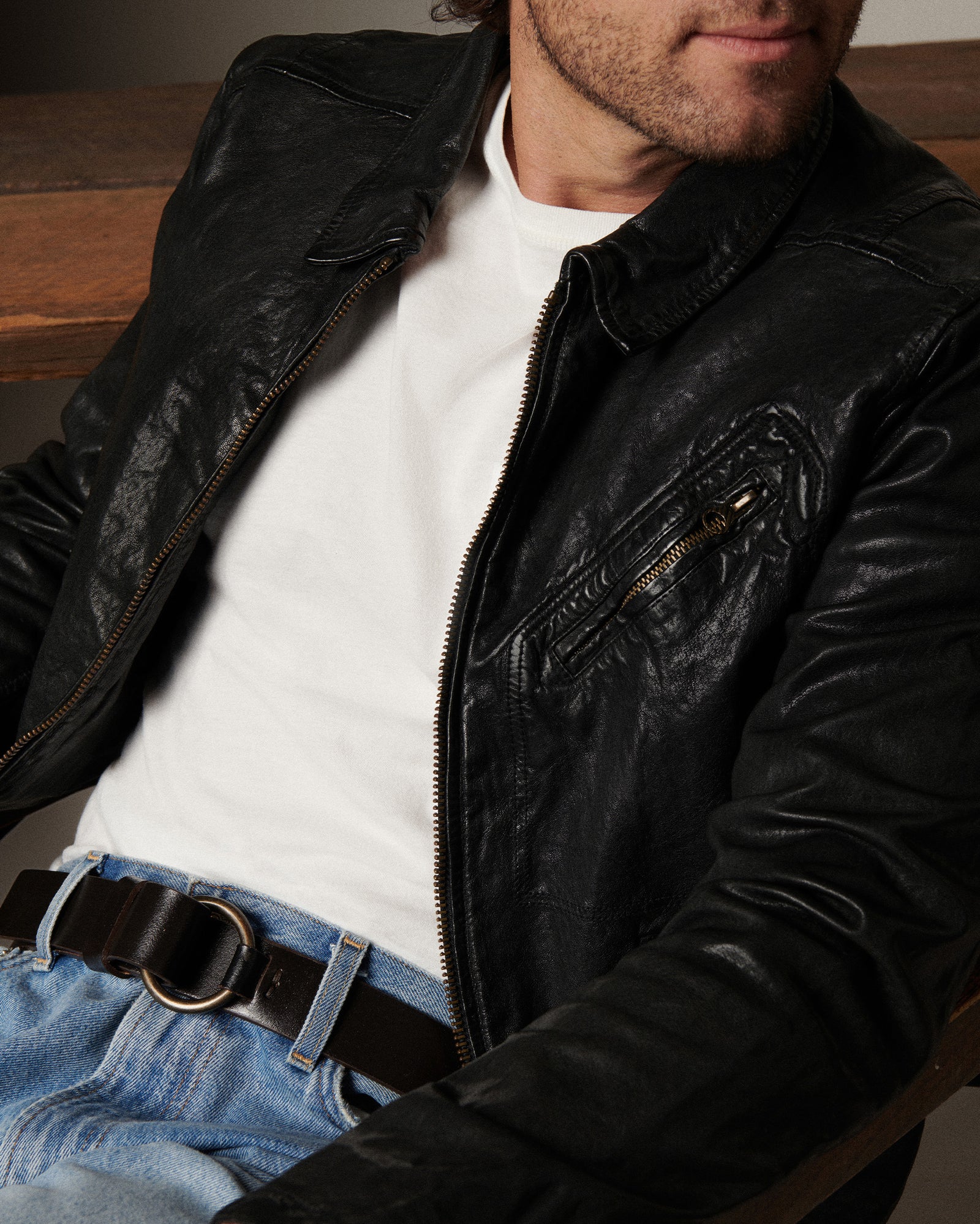 Man wearing a black leather jacket over a white shirt with a wooden background
