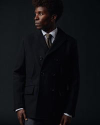 Man wearing a dark coat and tie against a black background