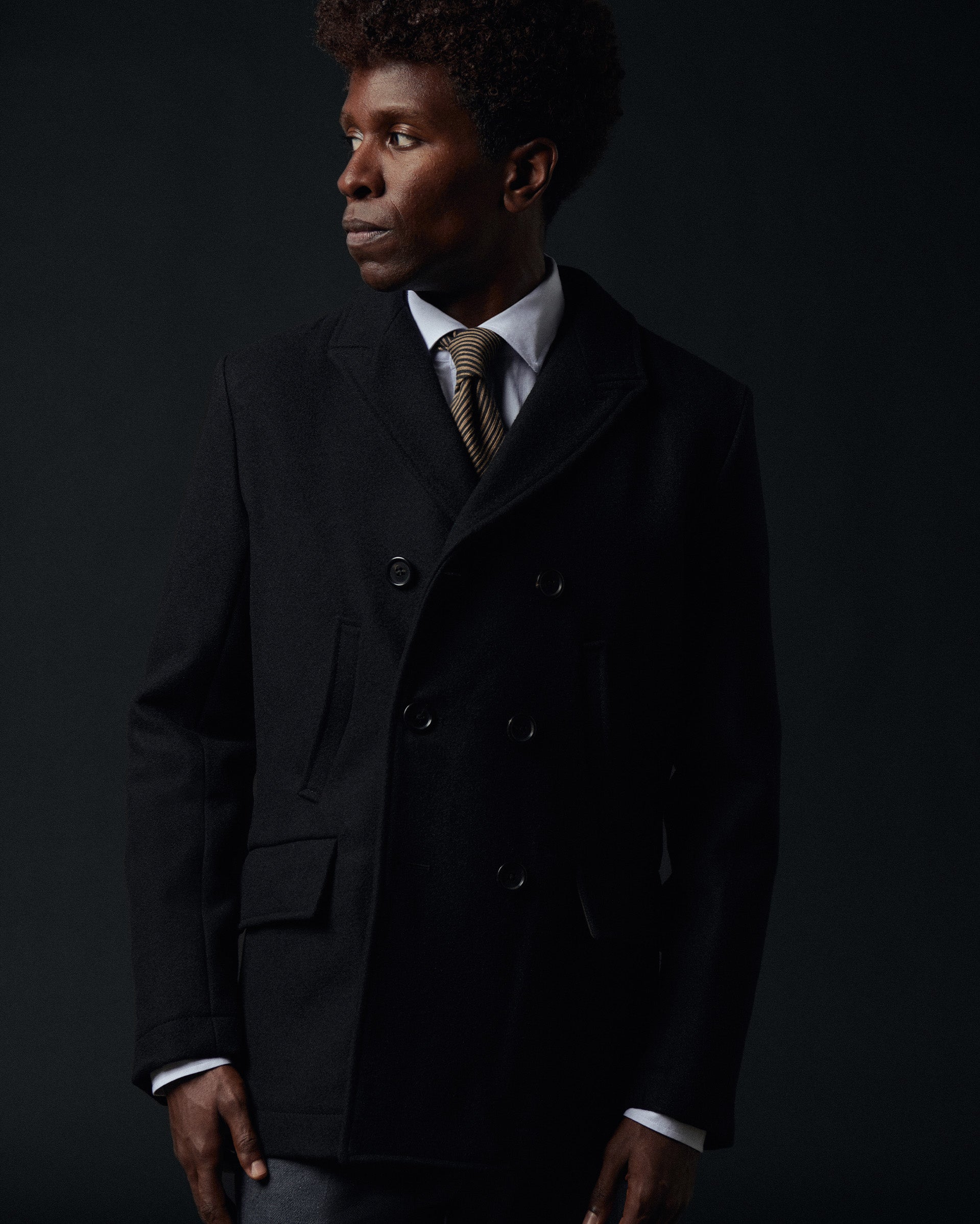 Man wearing a dark coat and tie against a black background