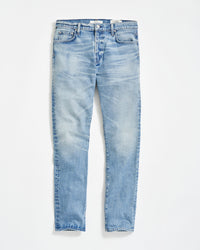 A pair of light blue, slim-fit jeans with a slight faded and worn effect, five pockets, and button fly, displayed flat on a white background.