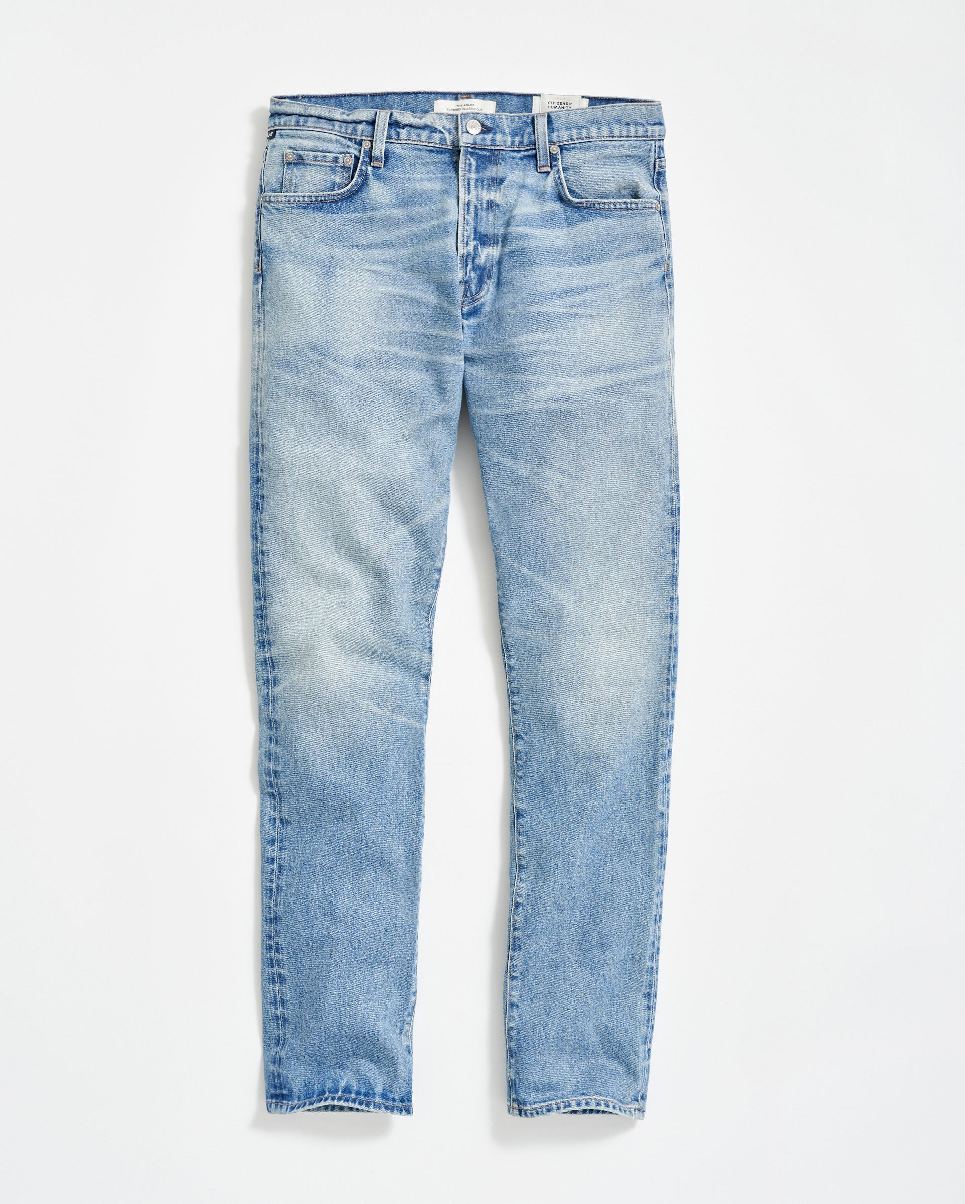 A pair of light blue, slim-fit jeans with a slight faded and worn effect, five pockets, and button fly, displayed flat on a white background.