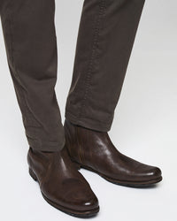 A person wearing dark brown leather ankle boots and dark brown pants, shown from the knees down against a plain, light-colored background.