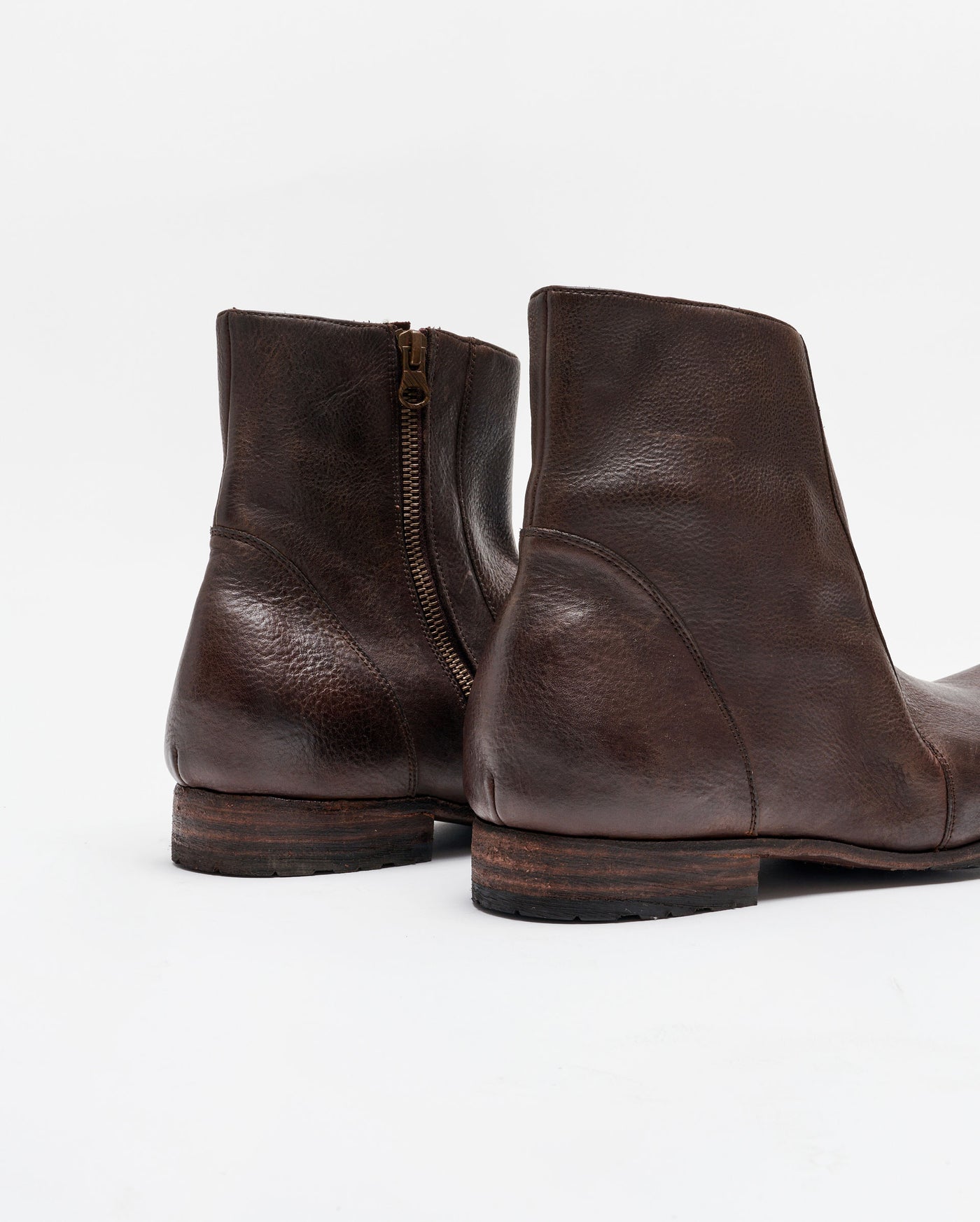 A close-up view of a pair of dark brown leather ankle boots with wooden soles, side zippers, and visible texture on the leather, set against a plain white background.