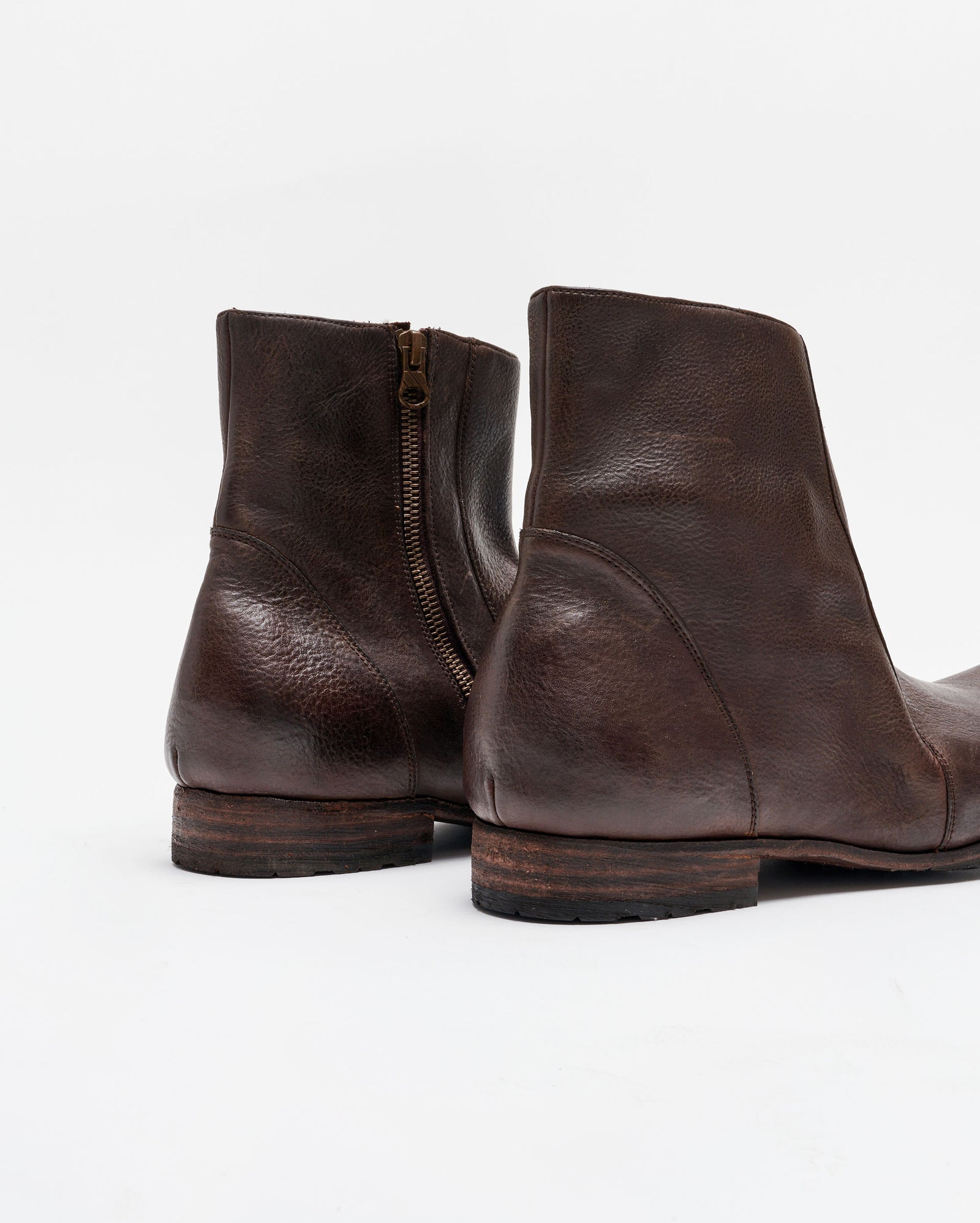 A close-up view of a pair of dark brown leather ankle boots with wooden soles, side zippers, and visible texture on the leather, set against a plain white background.