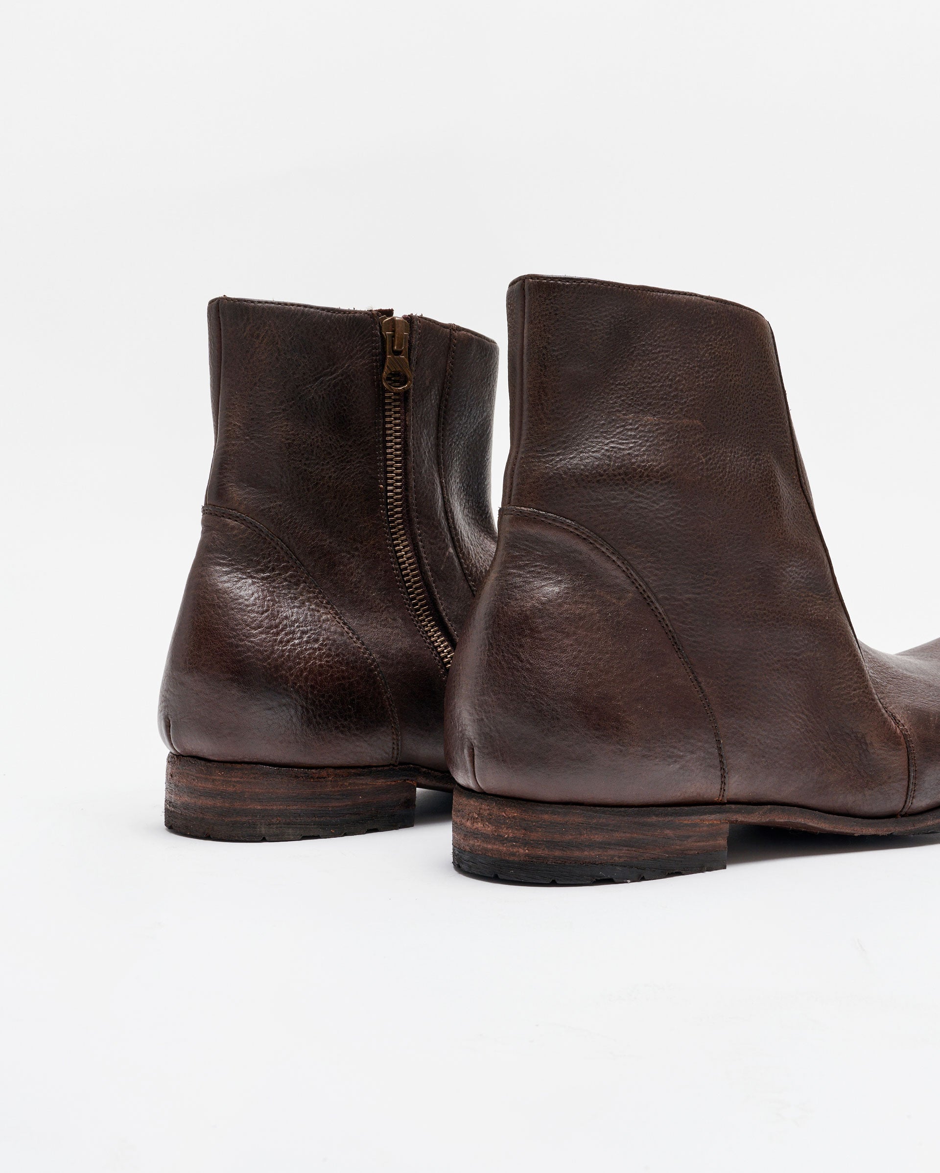A close-up view of a pair of dark brown leather ankle boots with wooden soles, side zippers, and visible texture on the leather, set against a plain white background.