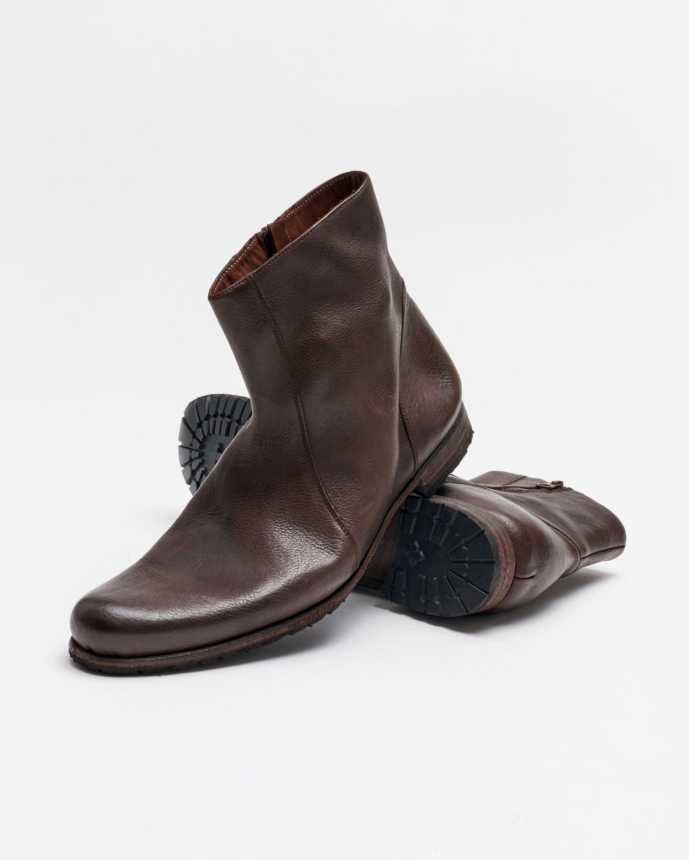 A pair of brown leather ankle boots with side zippers, one boot standing upright and the other lying on its side, showing the textured rubber sole. The background is plain white.