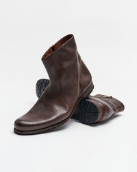 A pair of brown leather ankle boots with side zippers, one boot standing upright and the other lying on its side, showing the textured rubber sole. The background is plain white.