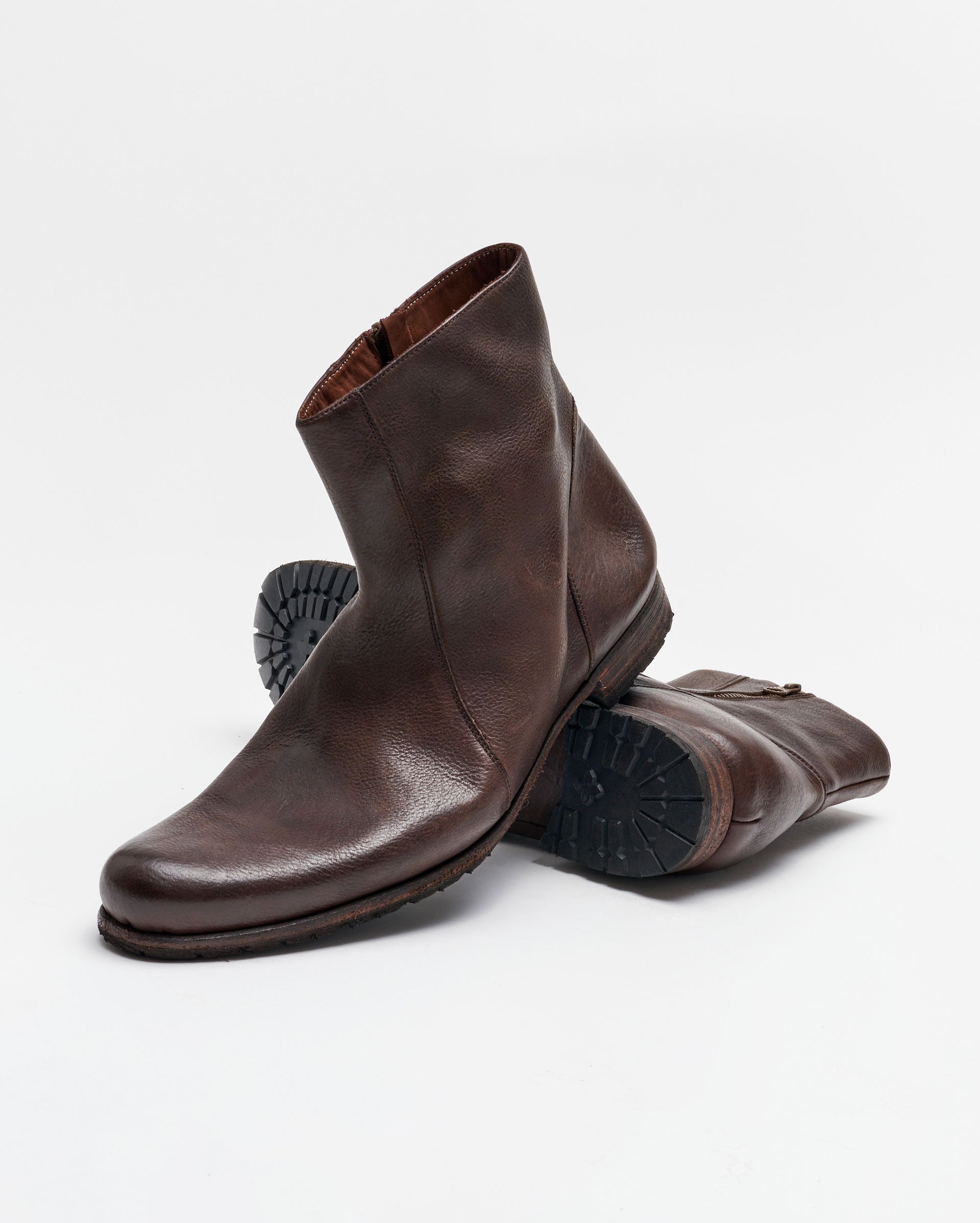 A pair of brown leather ankle boots with side zippers, one boot standing upright and the other lying on its side, showing the textured rubber sole. The background is plain white.