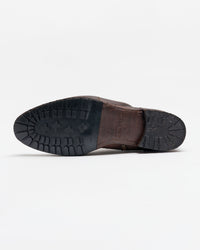 A brown leather shoe lying on its side, showing the black rubber sole with a rugged tread pattern, against a plain white background.