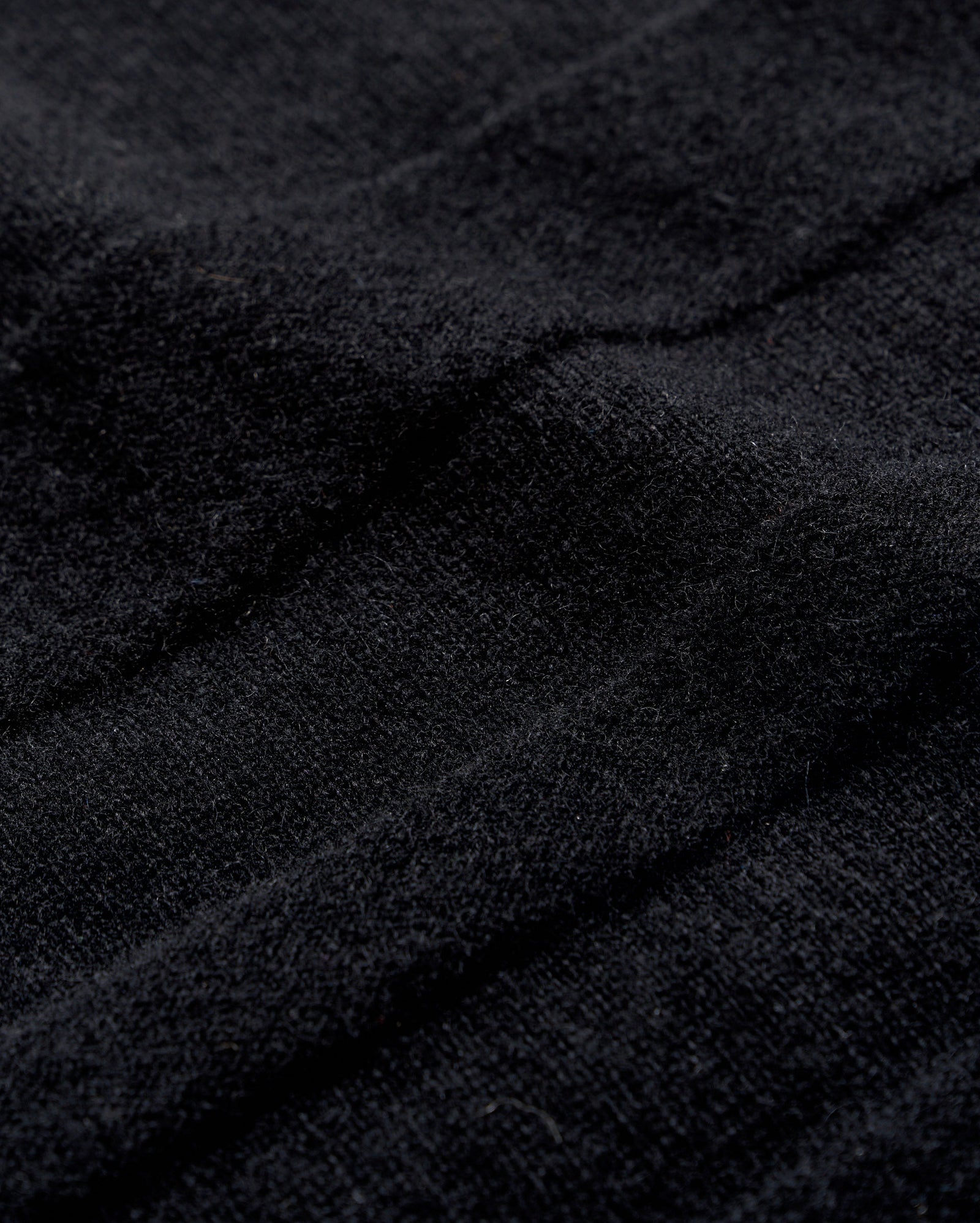 Close-up of black textured fabric with visible soft fibers and gentle folds, creating subtle shadows and depth across the surface.