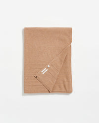 A neatly folded camel-colored blanket with visible tags on one corner, displayed on a white background.