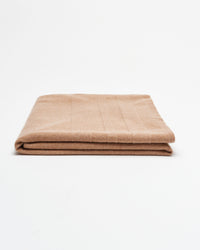 A neatly folded light brown blanket is placed on a plain white background.