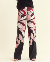 Person wearing wide-leg pants with a bold, abstract pink, red, black, and white floral pattern. Only the lower half of the body is visible; feet are in sandals and the background is light beige.
