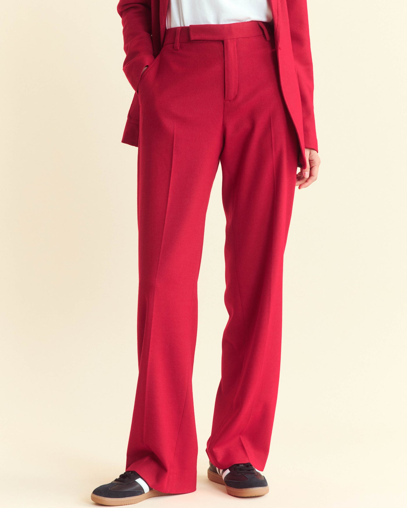 A person wearing high-waisted, wide-leg red trousers with a matching red blazer, white top, and black sneakers with white soles, standing against a light background.